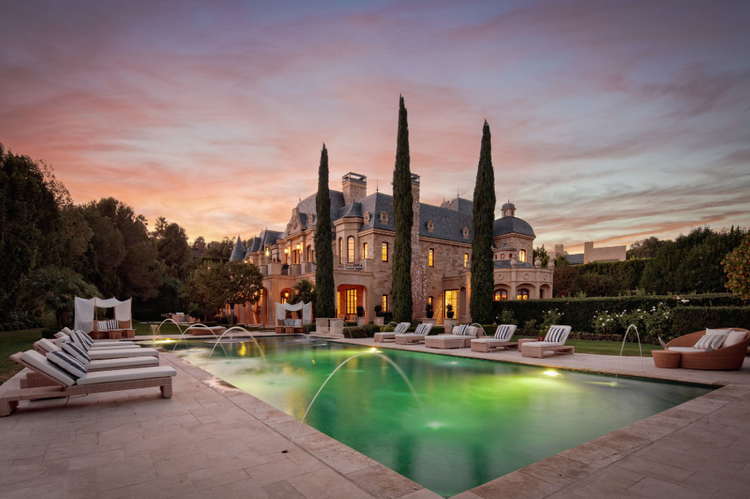French-style stone chateau with pool fountains under a sunset sky