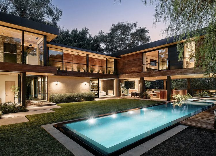 L-shaped wood-and-glass modern with pool and lawn at twilight