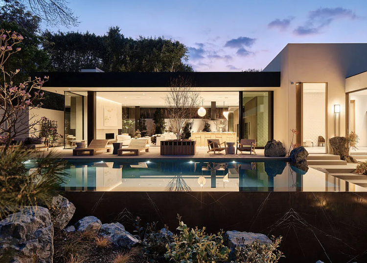 Glass pavilion living room glowing beside a reflecting pool at night