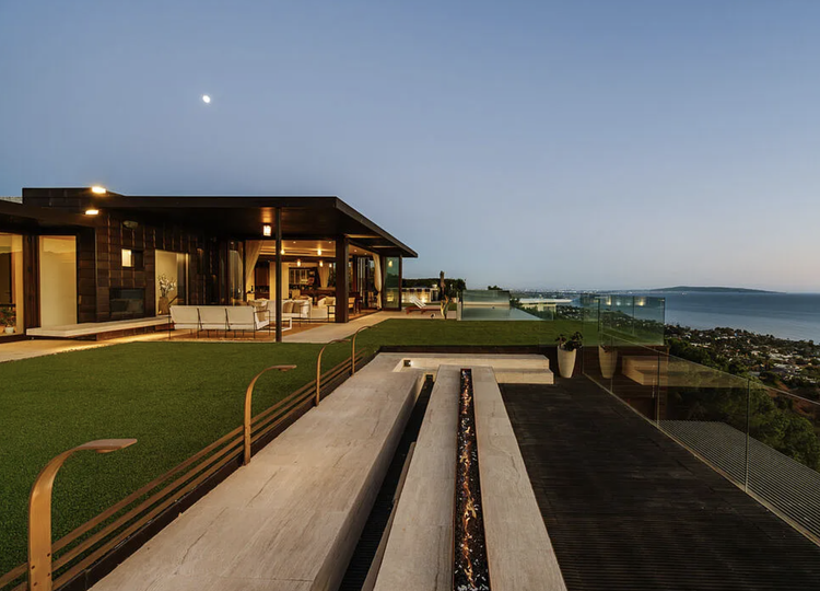 Modern flat-roof home with lawn and terrace overlooking the coastline at dusk