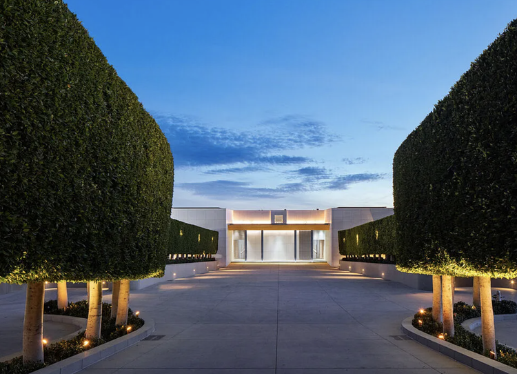 Sculpted hedges flanking the entry of a white modern home at dusk