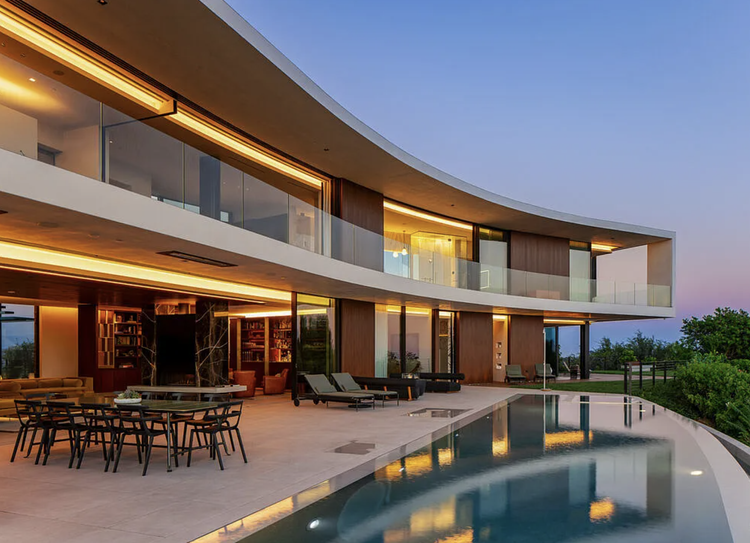 Curved modern home with warm wood interior and pool at dusk