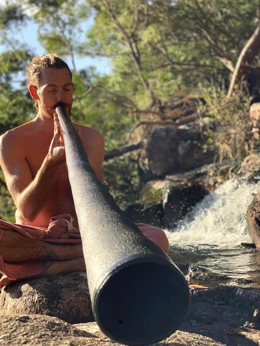 Mike Watts playing the didjeridu by a creek