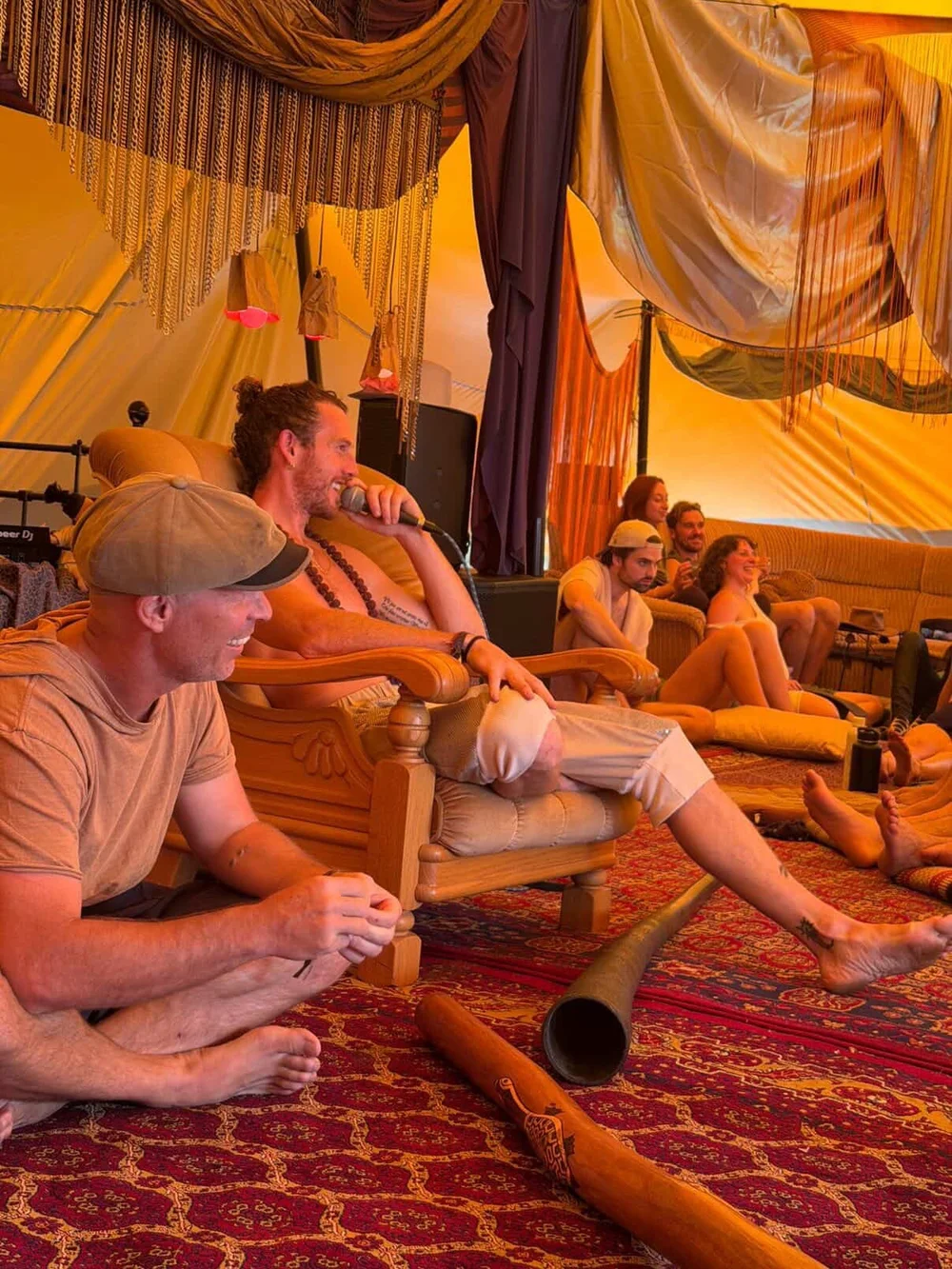Mike Watts speaking to a group in a festival tent, didjeridus at his feet