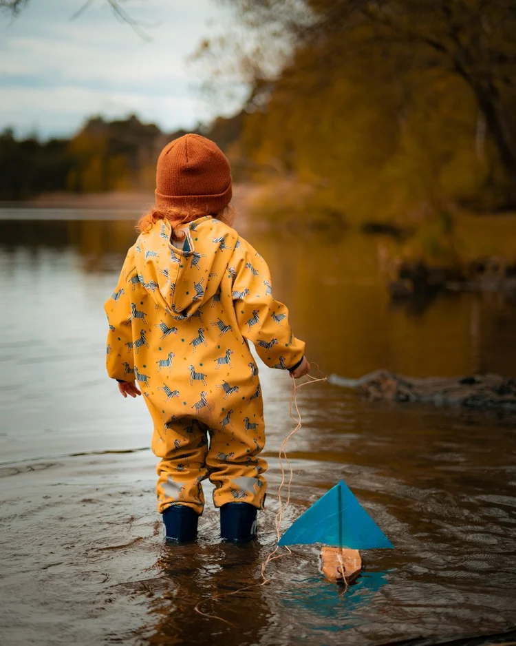 Child in a yellow raincoat by the water in autumn light