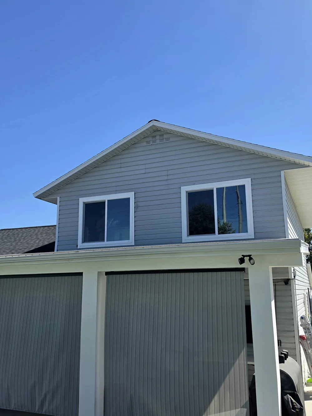 Two white sliding replacement windows above a porch on a gray-sided home, photographed by Windows Direct
