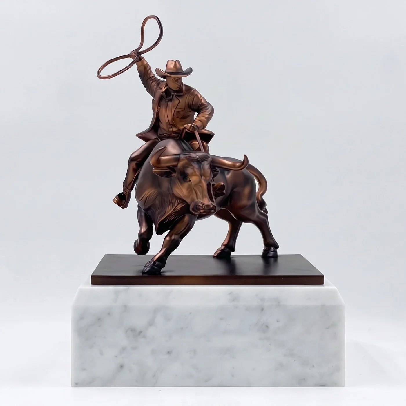 Fully sculptural deal marker featuring a bronze-finish cowboy riding a bull with a lasso on a white base.