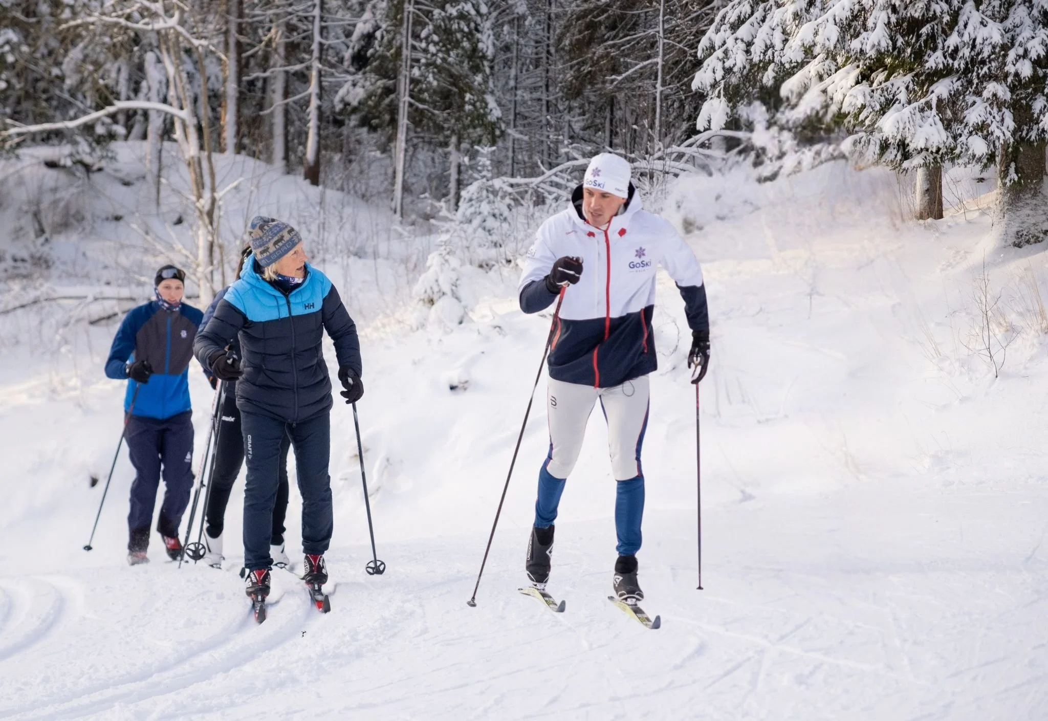 Instruktør forklarer klassisk skiteknikk til deltaker med rød sekk i skogen