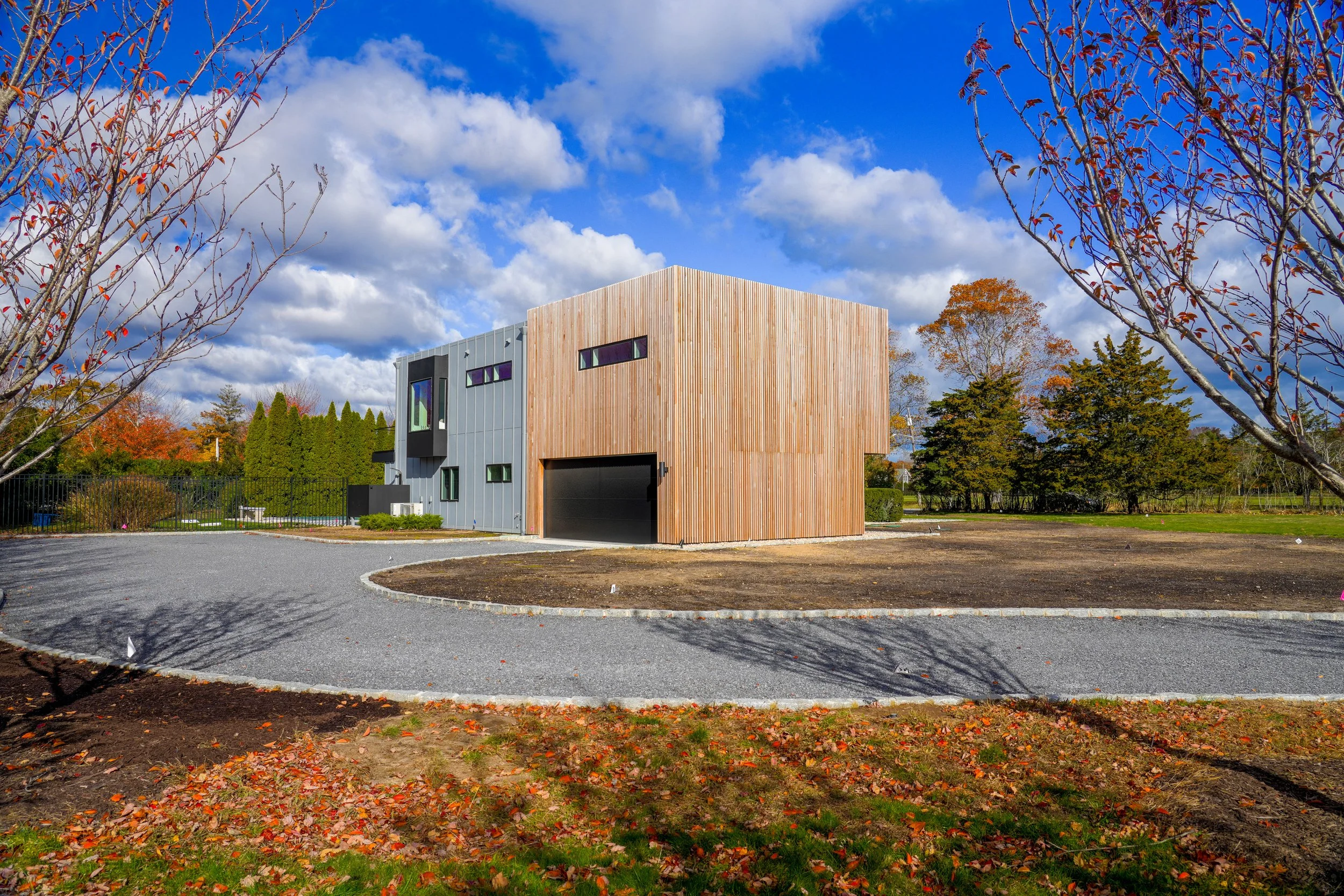 Modern wood-clad and gray building framed by autumn trees.