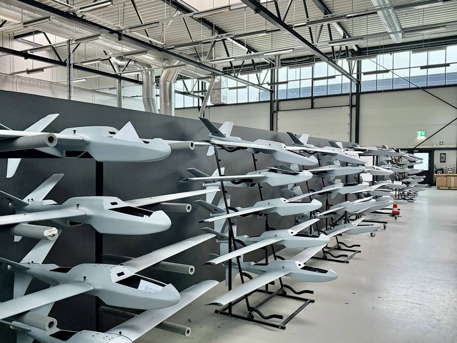 Rows of fixed-wing drones on storage racks inside the Robot Aviation production hangar.