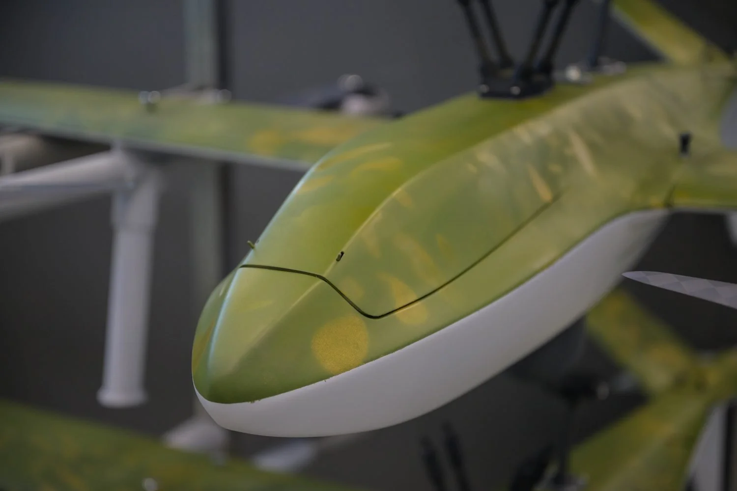 Close-up of a green camouflage drone fuselage in the Robot Aviation workshop, with more airframes behind.