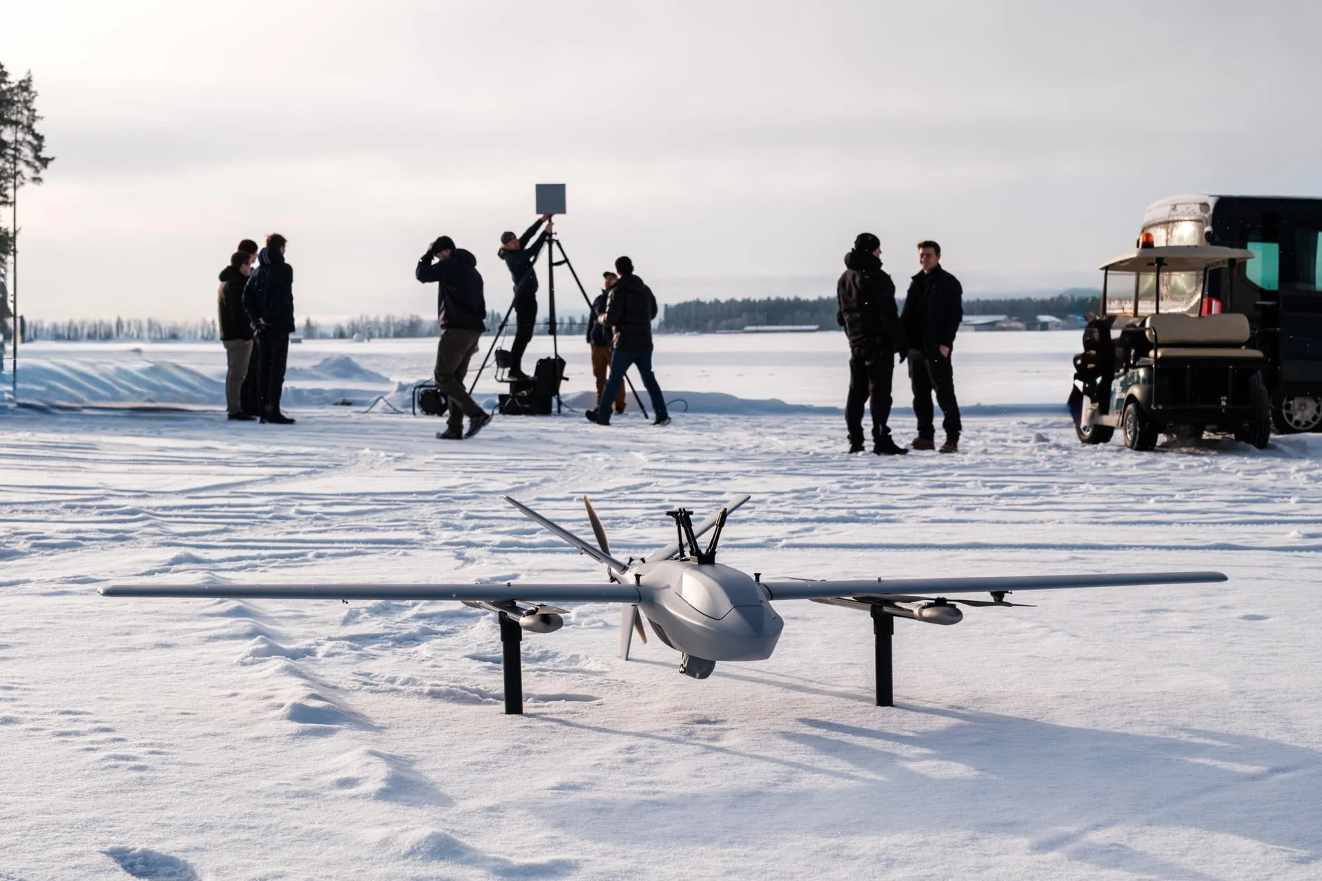 Robot Aviation team members and a film crew gathered around a drone on a snow-covered field.