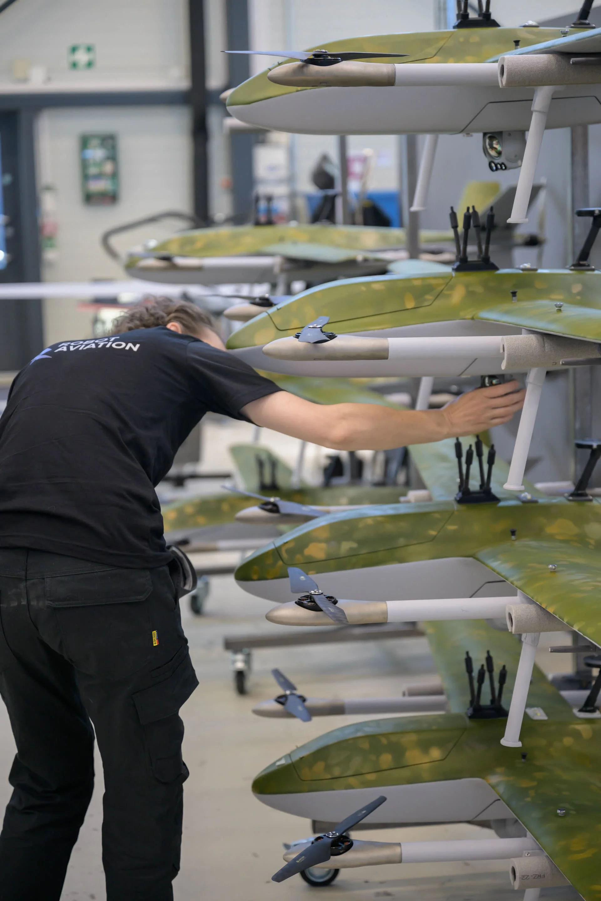 Technician inspecting a row of folded drone wing assemblies in the workshop.
