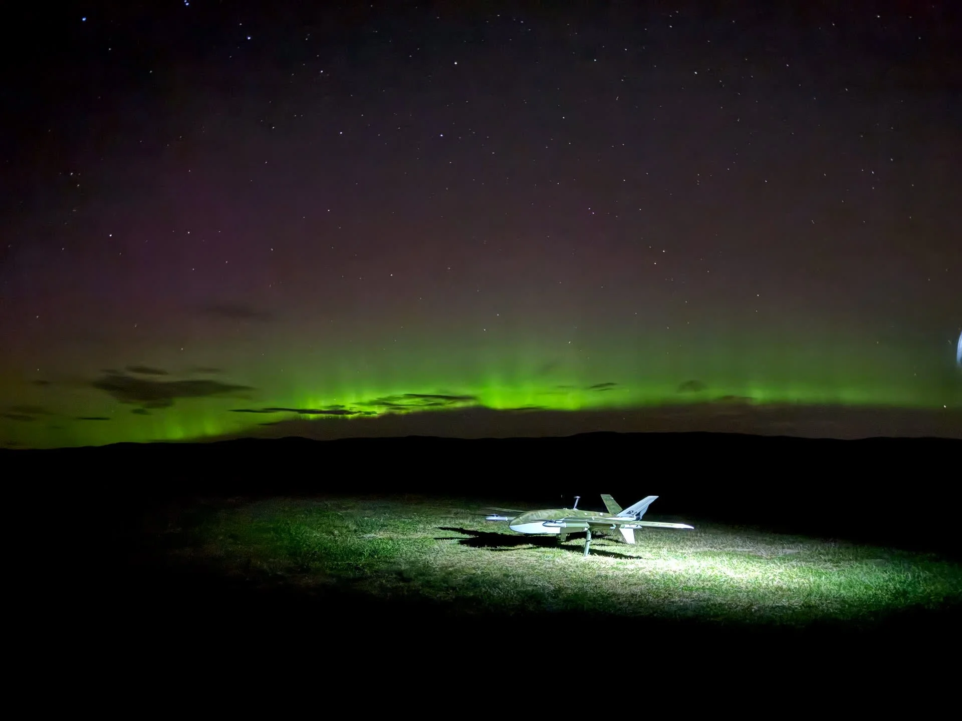 A Robot Aviation drone on the ground at night under the aurora borealis.