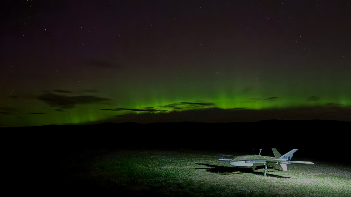 A drone on the ground beneath the aurora borealis at night.