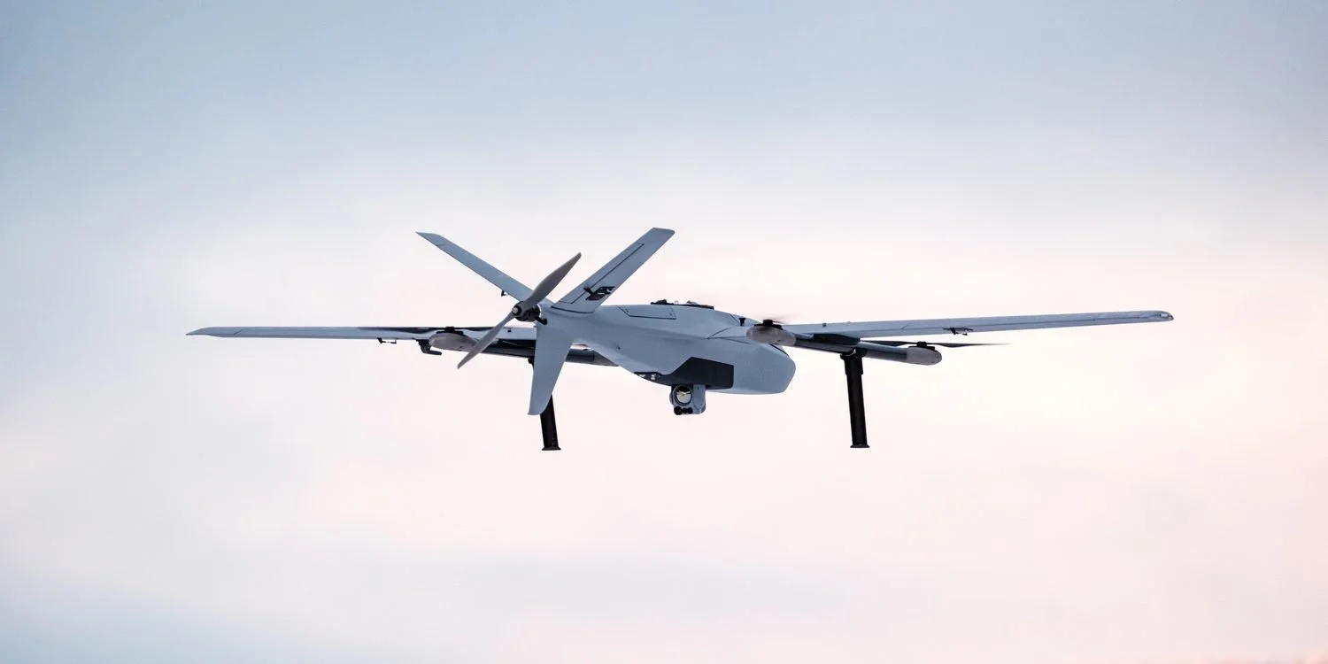 A Robot Aviation fixed-wing VTOL drone with an electro-optical gimbal in flight against a pale sky.
