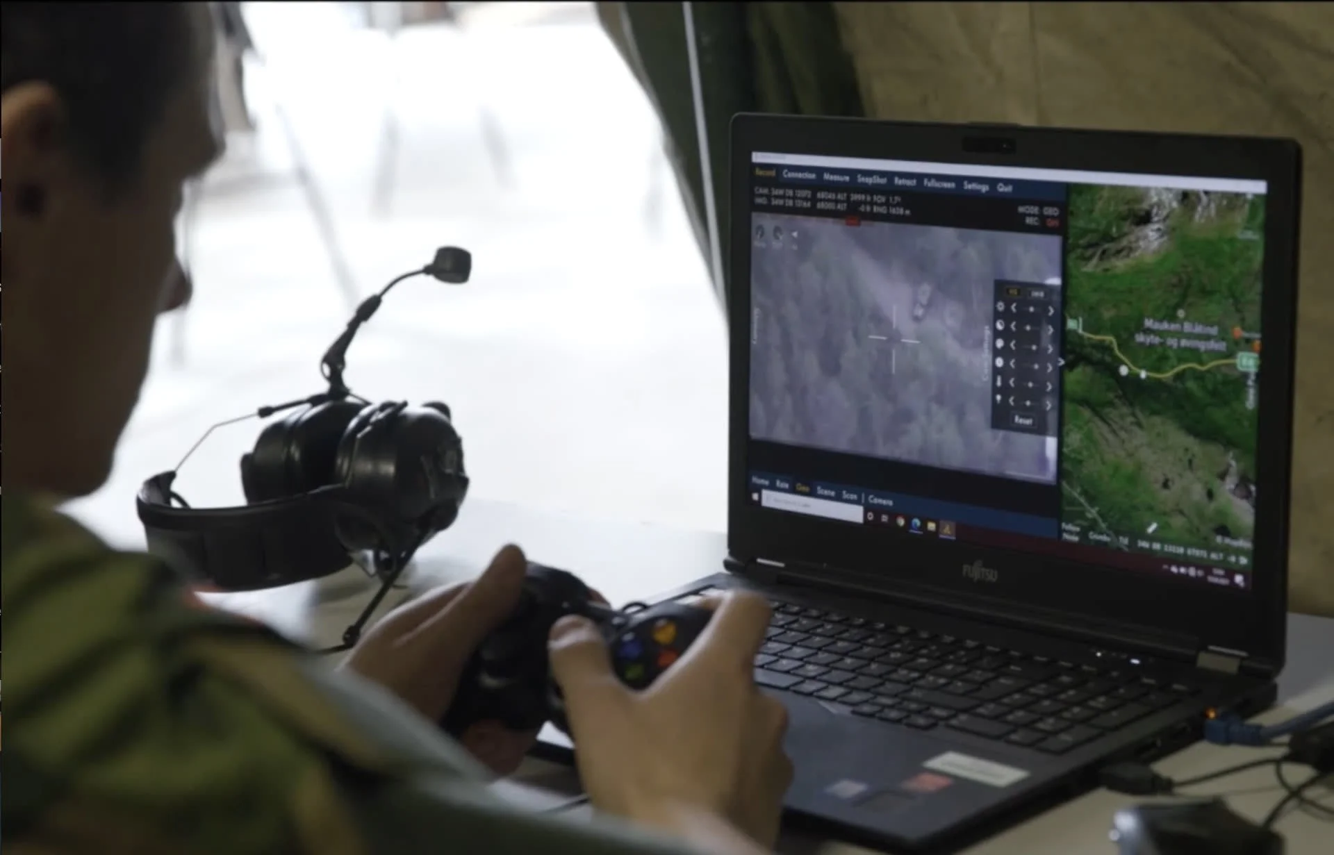 Operator using a handheld ground control device to monitor a surveillance drone's live map feed.