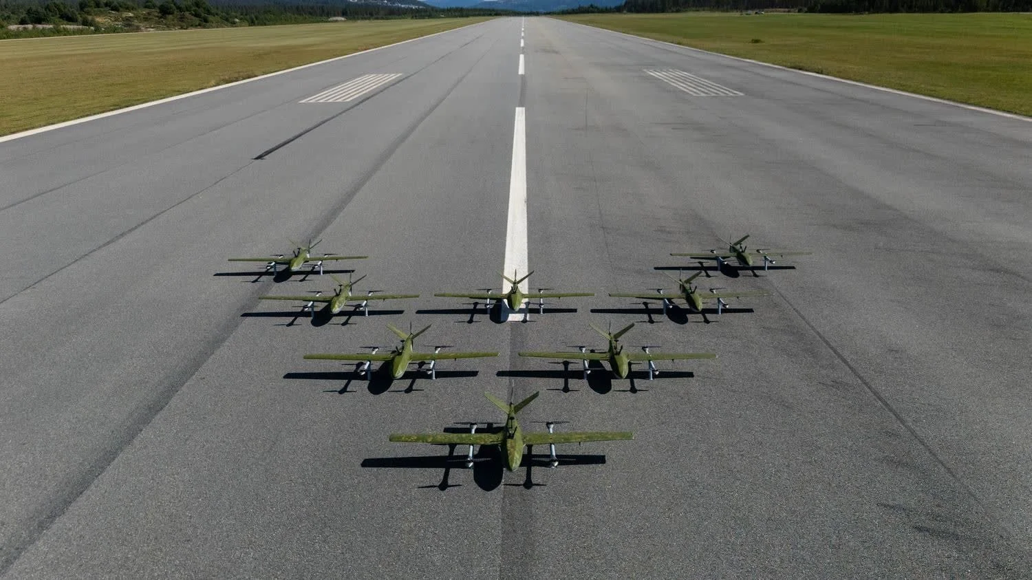 Multiple fixed-wing drones lined up on a runway.