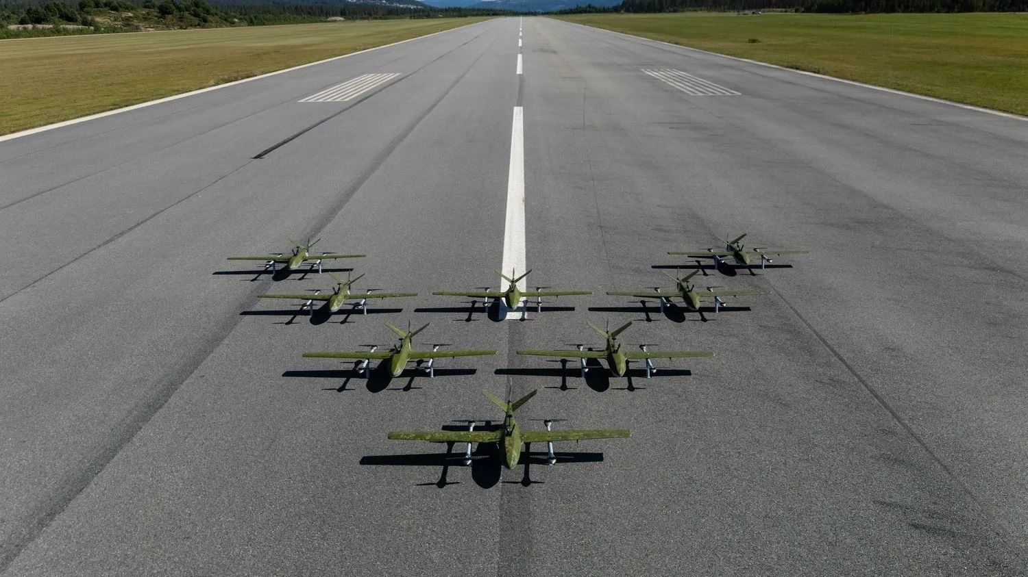 A formation of green fixed-wing Robot Aviation drones arranged on an airfield runway.