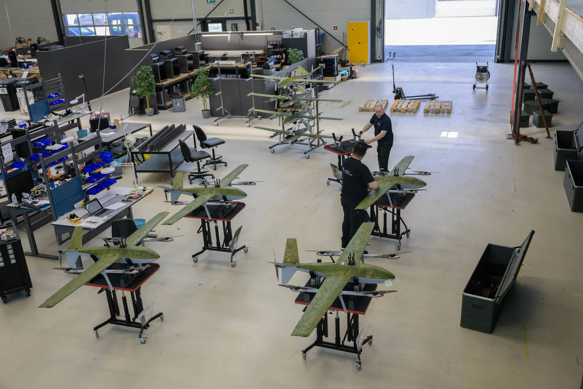 Overhead view of the production floor with multiple drone airframes on assembly stands.