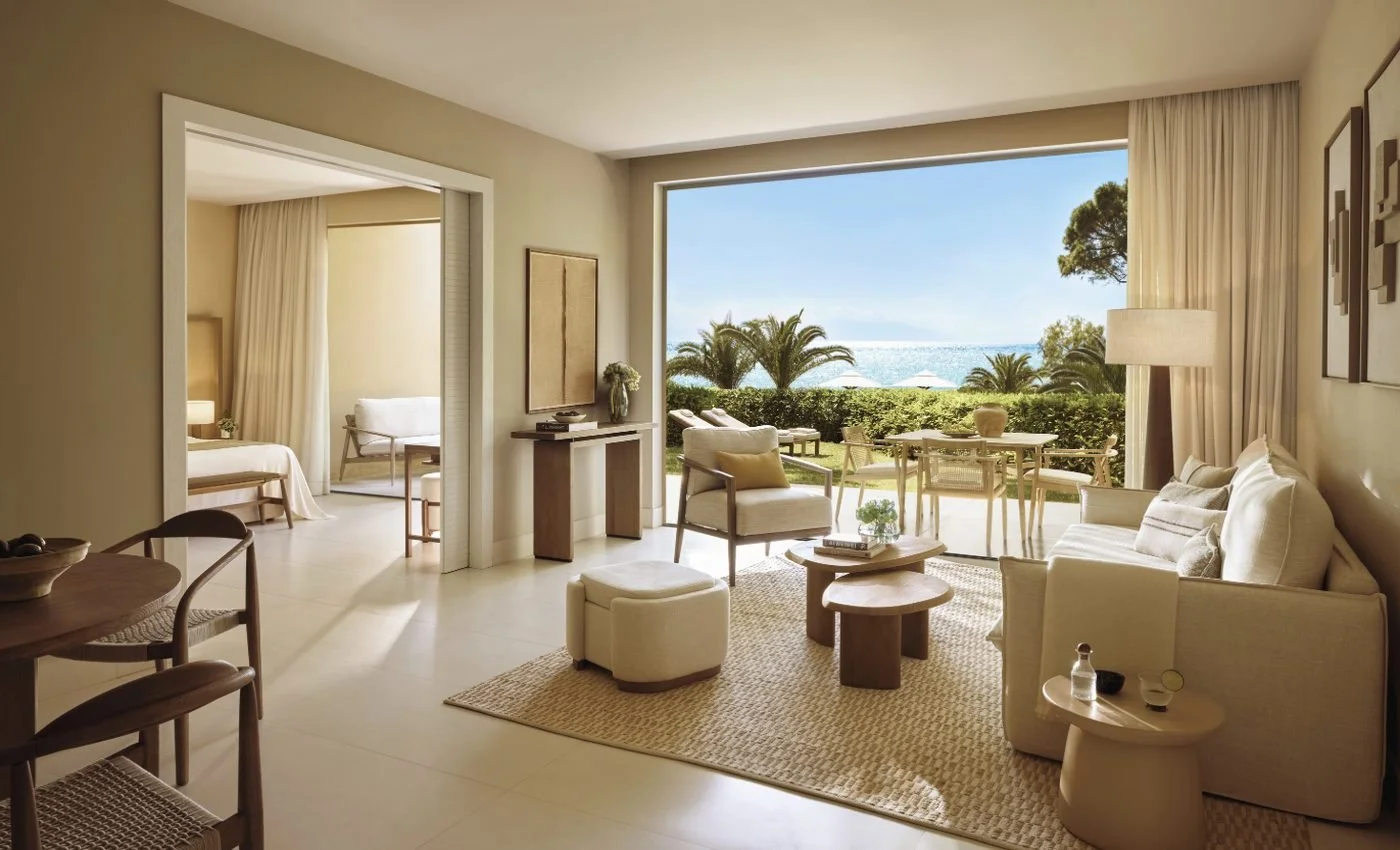 Living room of a two-bedroom suite at Sani Club opening onto a private garden with palms and the sea beyond