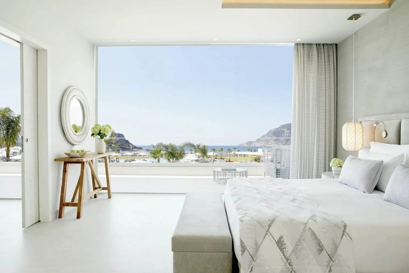 The bedroom of a Deluxe One Bedroom Bungalow Suite at Ikos Aria with a picture window over palms and the bay