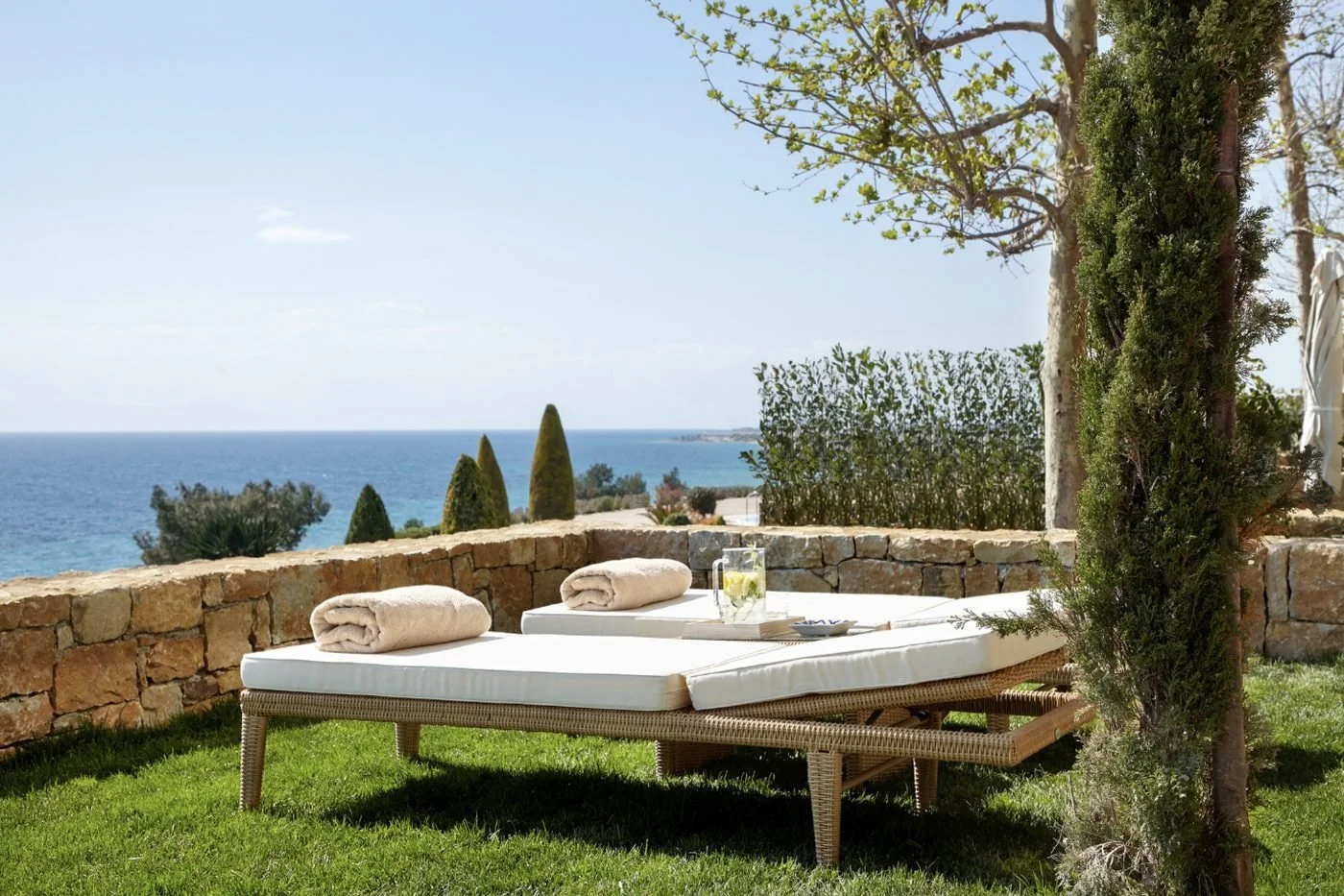 Sun loungers on the lawn of a Deluxe Junior Suite Private Garden, with cypress trees and the sea beyond