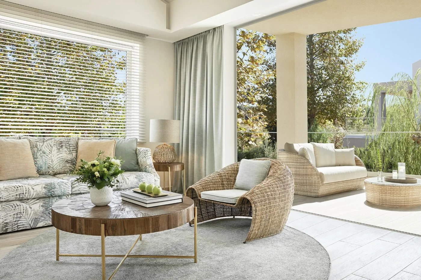 The living room of a One Bedroom Suite Grand Balcony opening onto a covered balcony with wicker sofas and trees