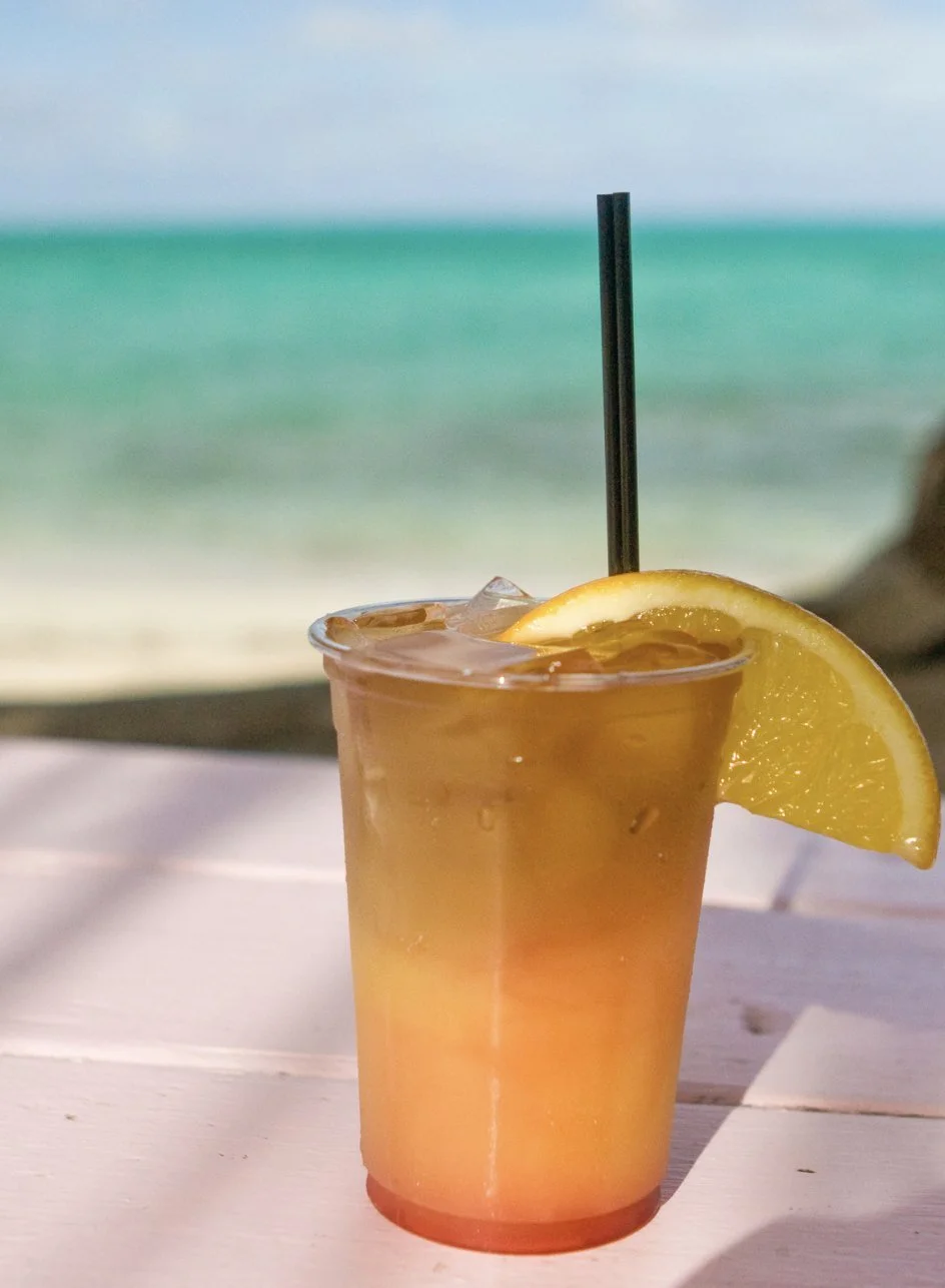 A golden rum punch over ice with a slice of orange, on a beach bar table by the sea