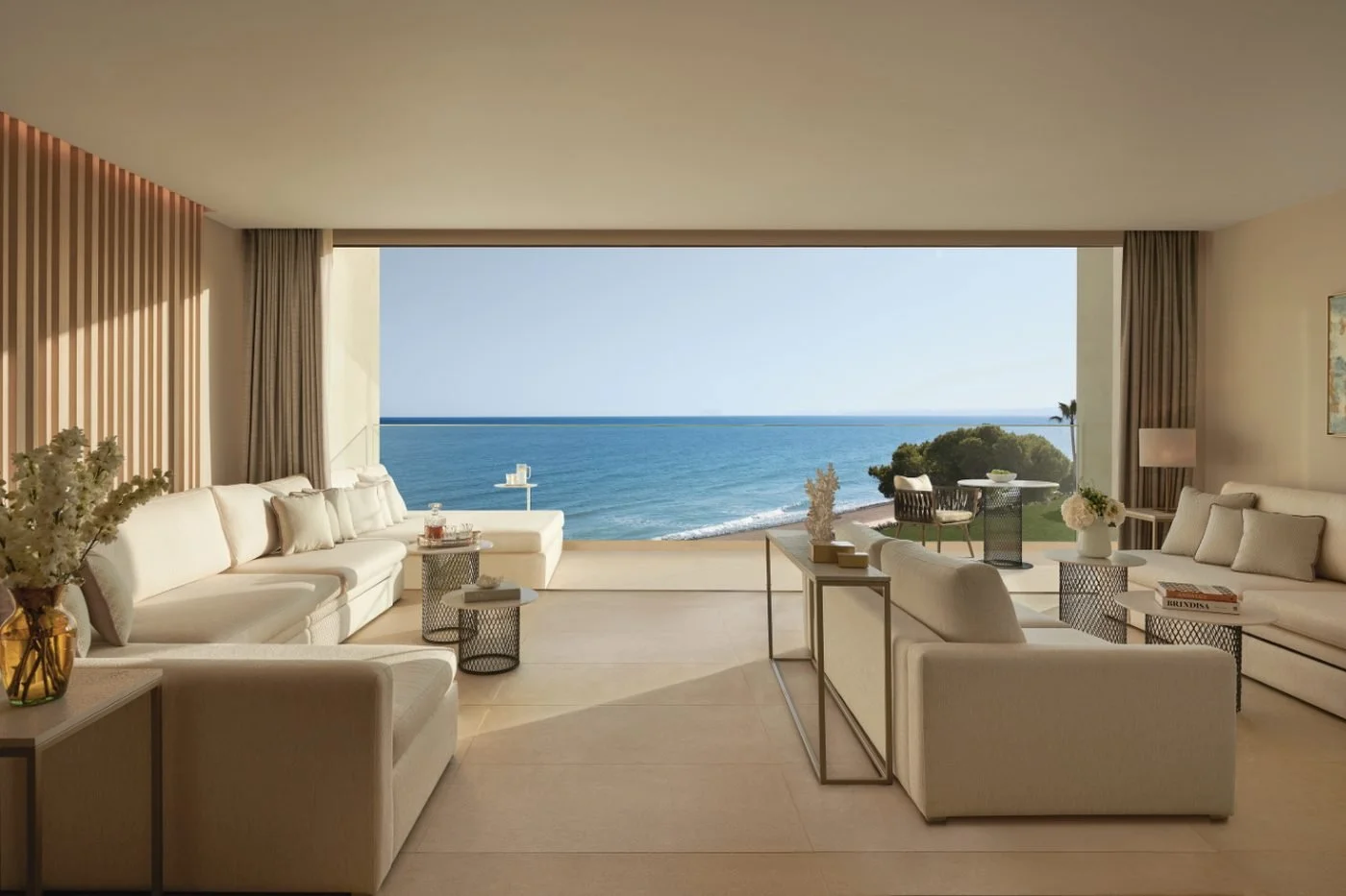 The living room of a Deluxe Two Bedroom Suite with deep sofas and a wide opening onto the sea