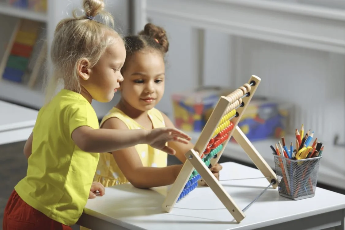 Two little girls playing together with a wooden abacus at a kids' club table