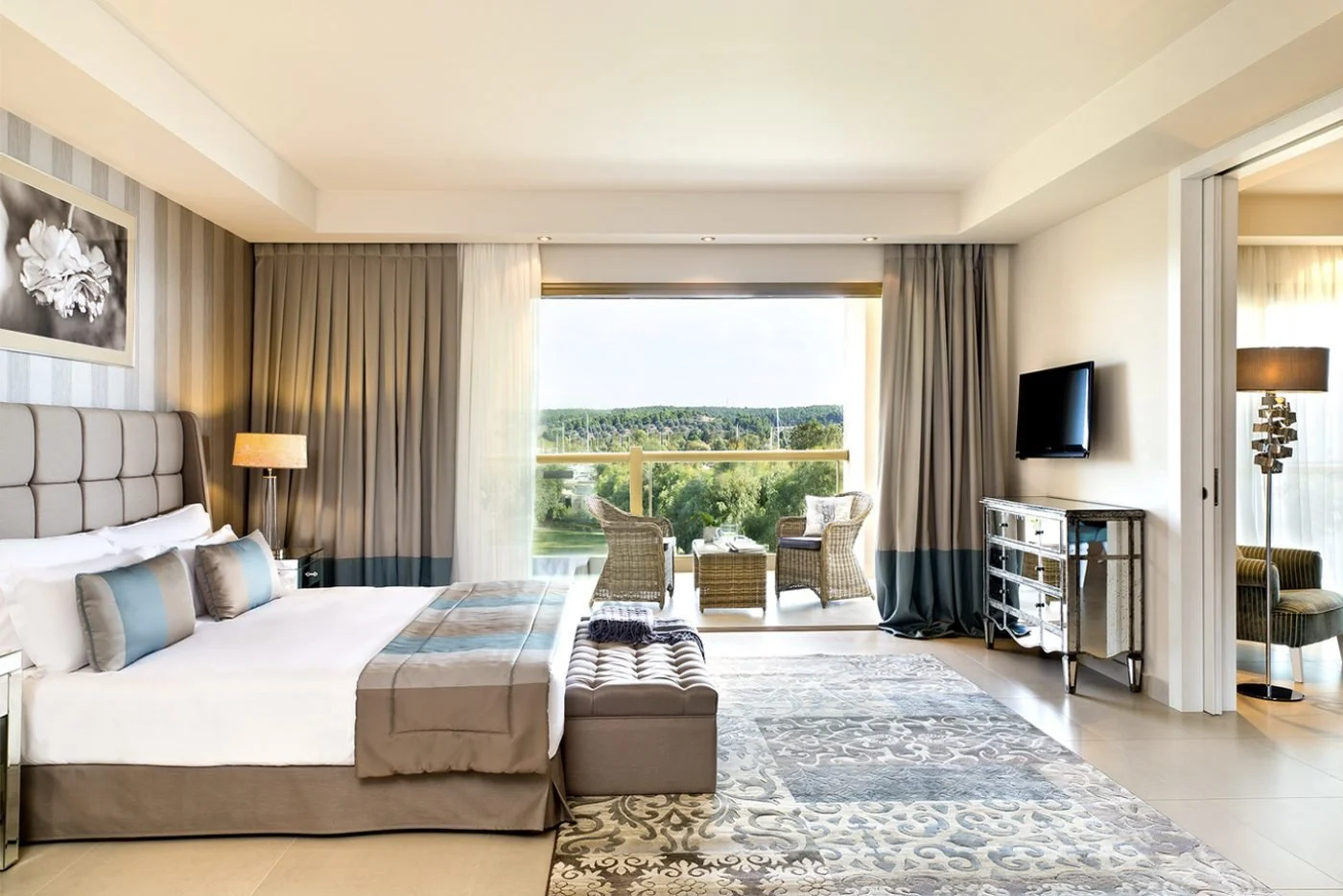 The bedroom of a Deluxe One Bedroom Family Suite opening onto a balcony with rattan chairs