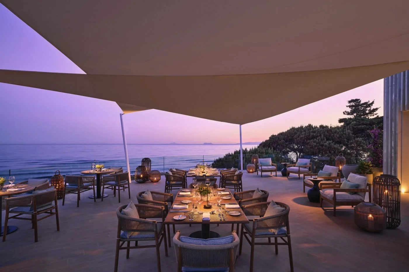 Tables set for dinner on the Seasons terrace at dusk, under white sails above the sea