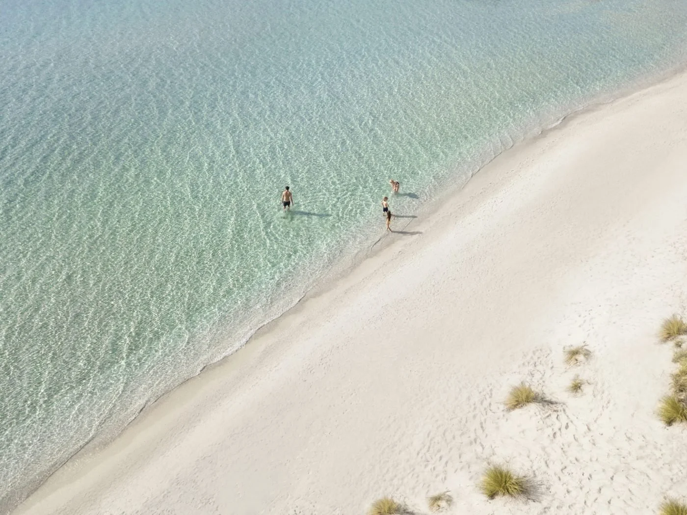 Looking down on a family paddling in clear, shallow water off the white sand of Bousoulas beach