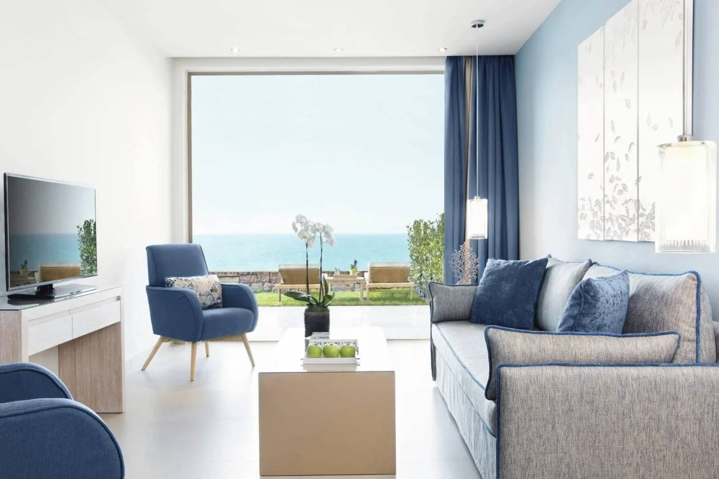 The lounge of a One Bedroom Family Suite at Ikos Oceania, with a terrace and the sea beyond