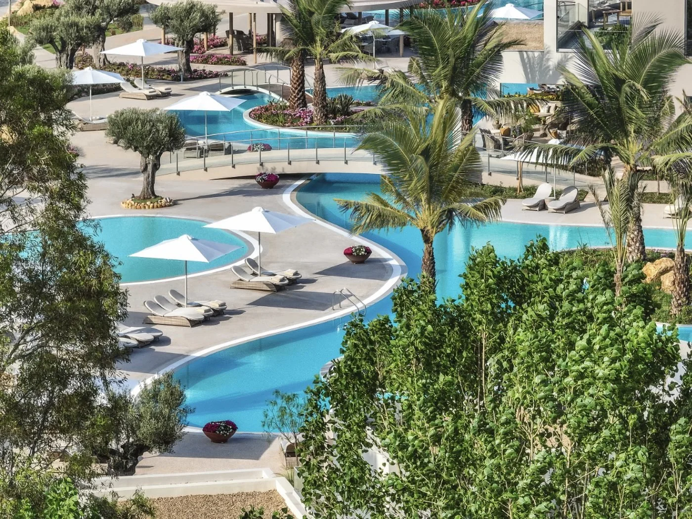Lagoon-style pools winding between palm trees, olive trees and sun loungers at Porto Sani