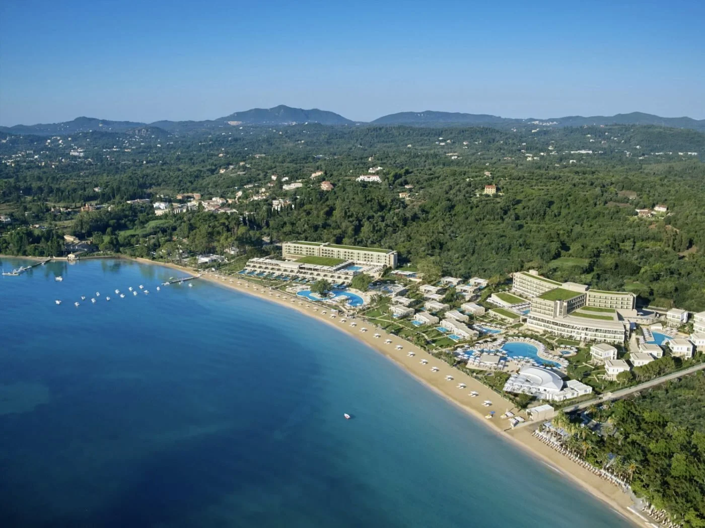 Ikos Dassia from the air, its buildings and pools set behind a long sandy beach on Corfu's green east coast