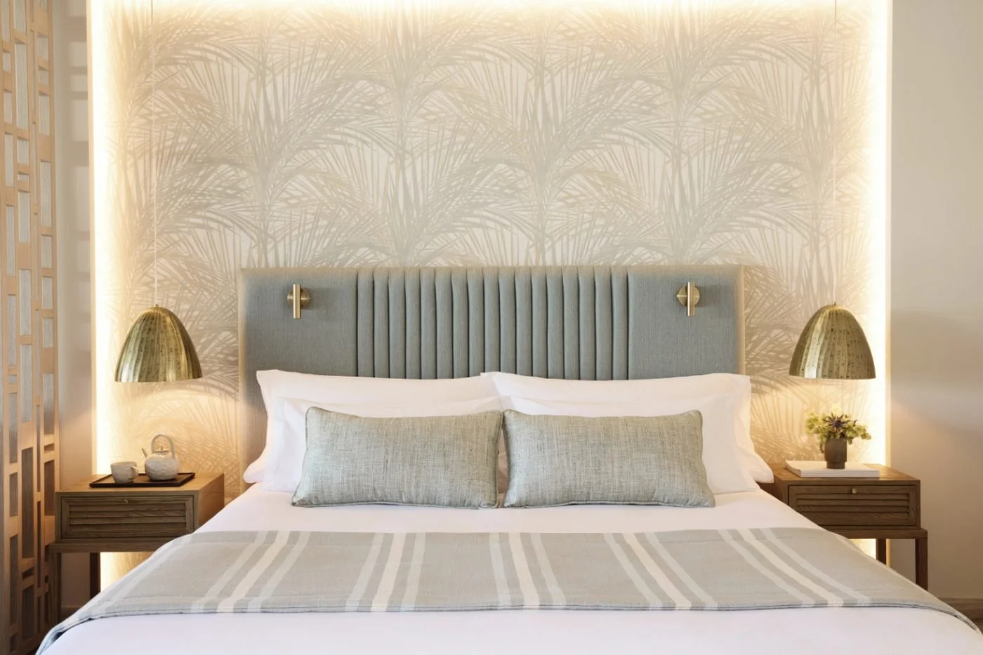A Junior Suite bed at Porto Sani with a sage green headboard, brass lamps and softly lit palm-print wallpaper