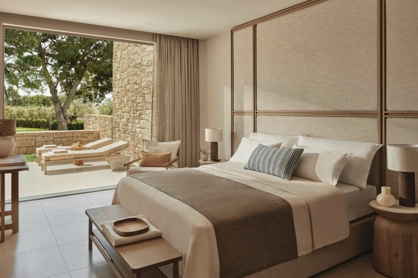 The bedroom of a Deluxe One Bedroom Bungalow Suite with Private Garden, its doors open to sun loungers under the pines