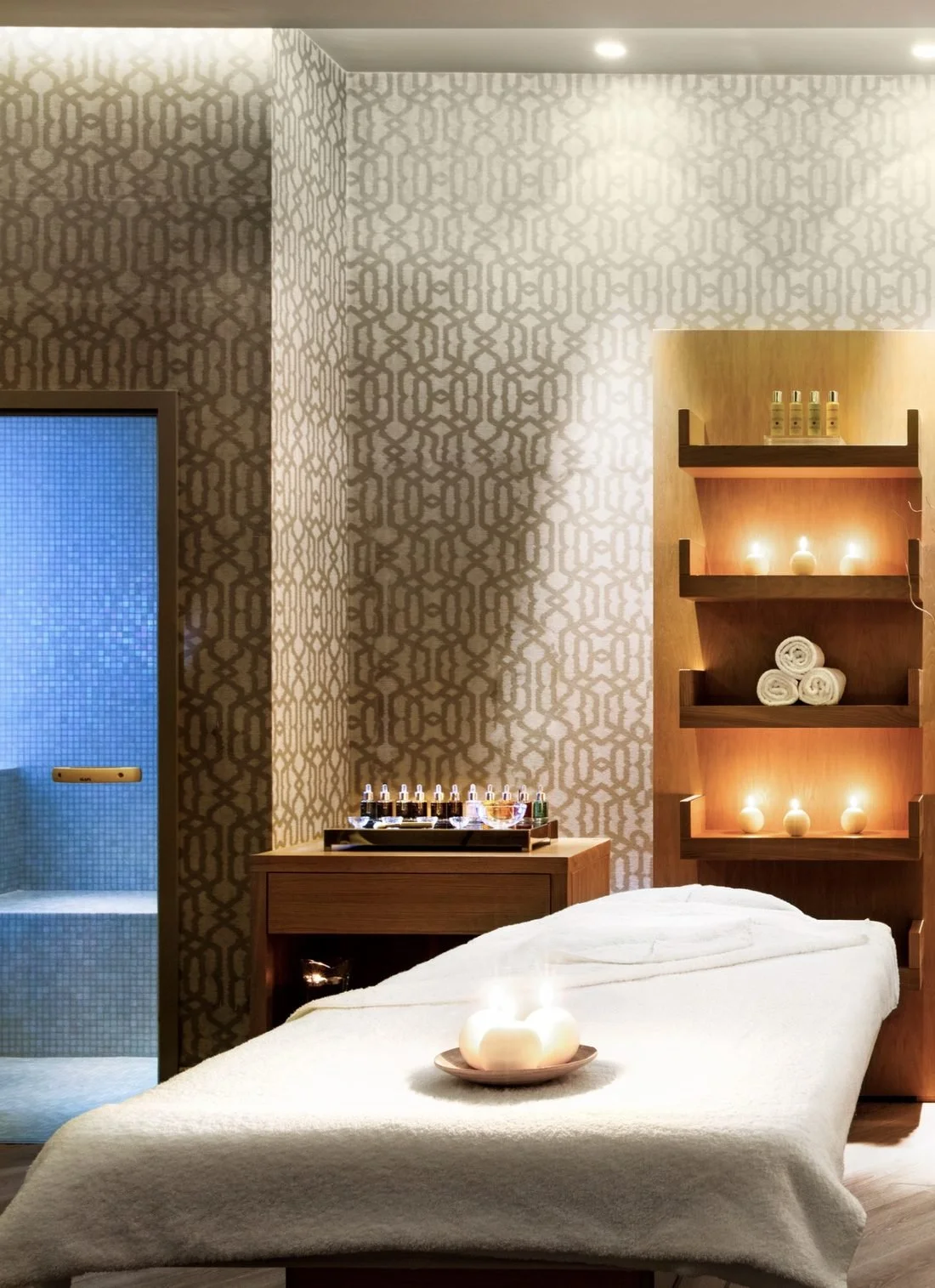 A candlelit treatment room at the Ikos Spa, with folded towels and a massage table