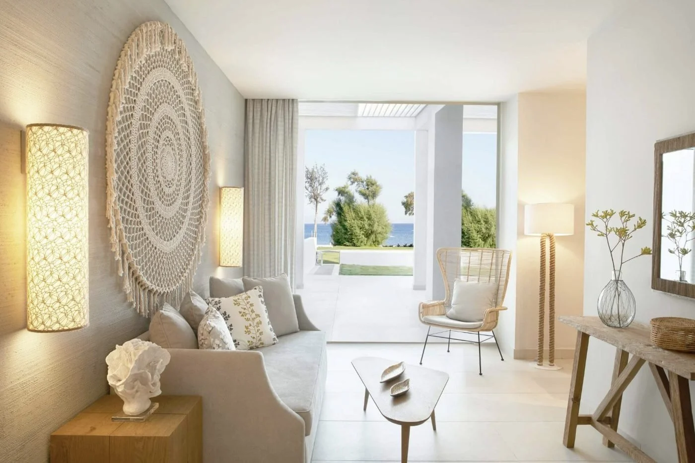 The living room of a Deluxe One Bedroom Bungalow Suite Beachfront at Ikos Aria opening onto a garden terrace and the sea