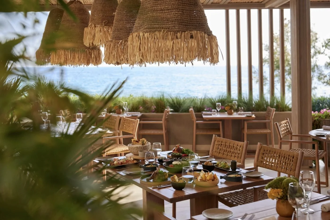 Sharing plates on a wooden table under woven lampshades at the Beach Club, looking out to sea