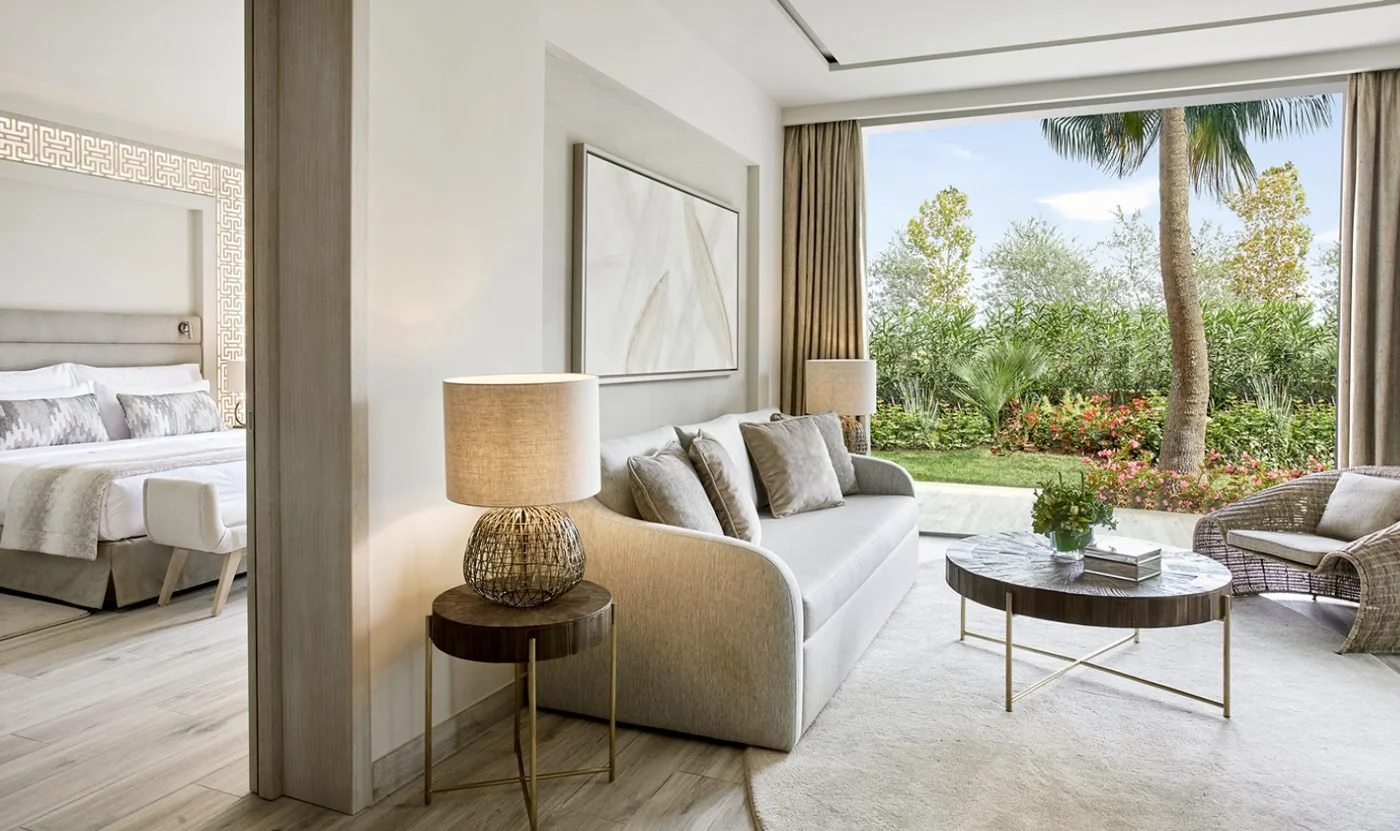 The living room of a One Bedroom Suite Private Garden opening onto a flowering garden, with the bedroom beyond