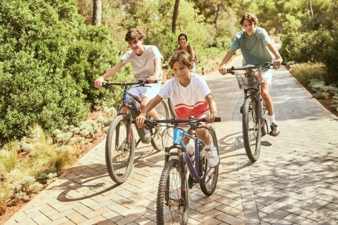 Three boys and a woman cycling along a paved path through the gardens