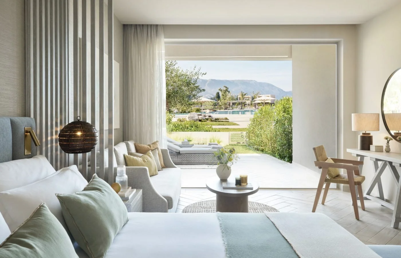A Junior Bungalow Suite Private Garden, with a sofa and bed facing open doors to the garden and pools