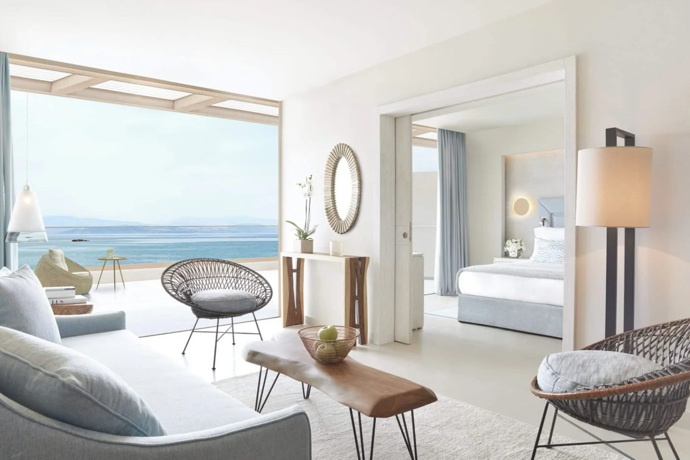The living room of a One Bedroom Suite opening onto a balcony with sea views, with the bedroom beyond