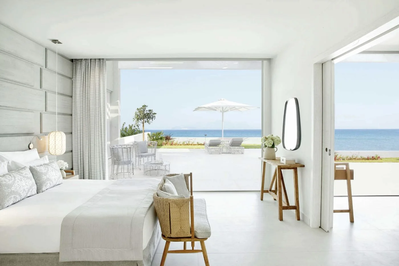 A bedroom in a Deluxe Two Bedroom Bungalow Suite Beachfront at Ikos Aria opening onto a terrace with loungers, a parasol and the sea