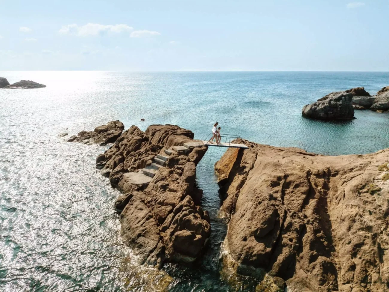 Two people crossing a small footbridge between rocks above the sea