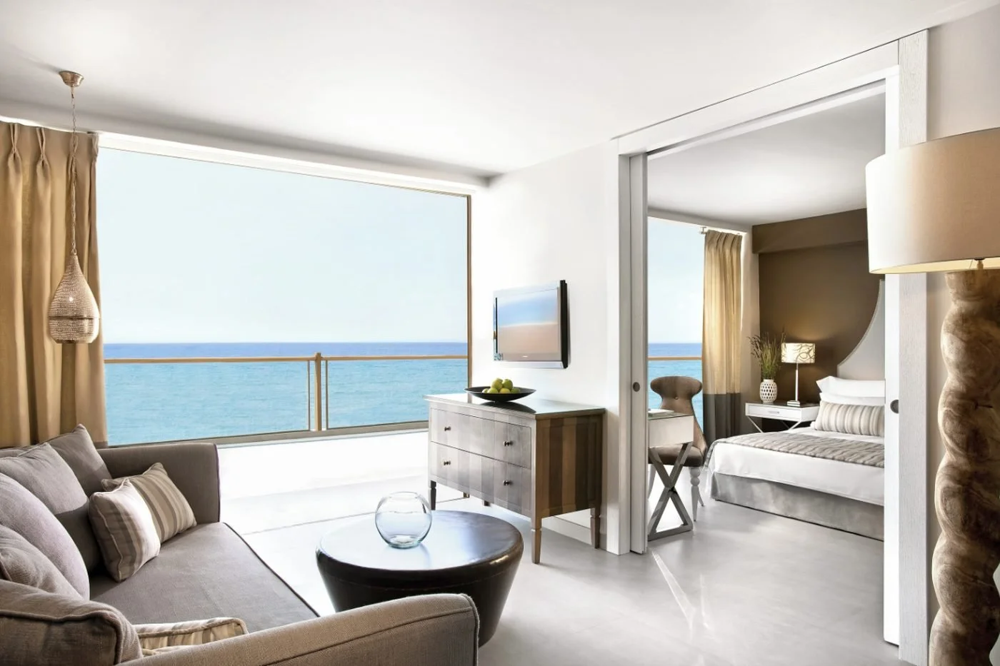 The living room of a One Bedroom Family Suite with a sea view balcony and the bedroom beyond