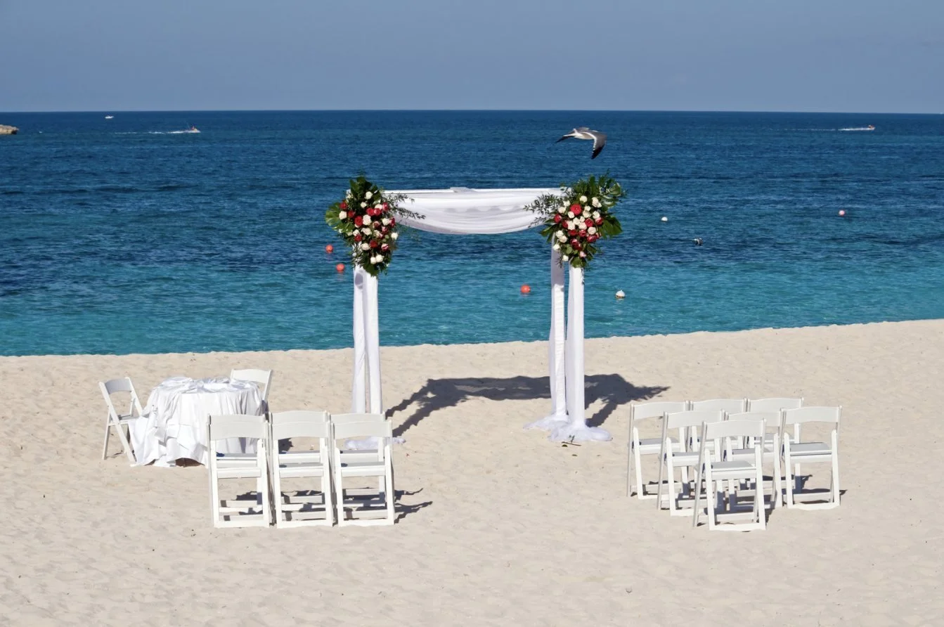 A flower-dressed wedding canopy and white chairs on a beach